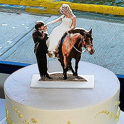 Photo cutout cake topper of bride on a horse and groom kissing her hand.Cake topper is sitting on a wedding cake.